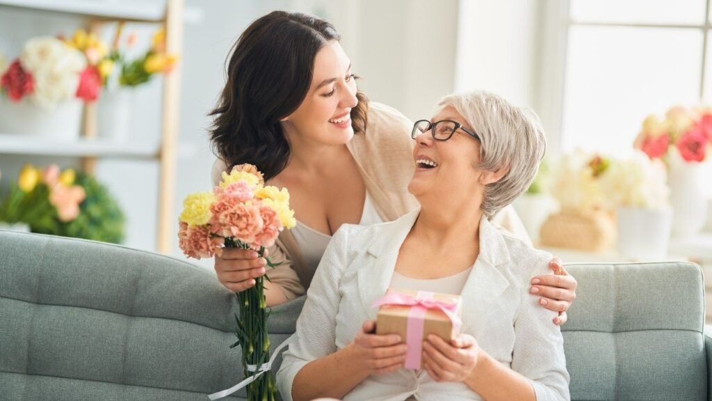 Banner comemorativo do Dia das Mães exibindo o Perfume Lancôme La Nuit Trésor, o Kit Taiff e fones de ouvido JBL sobre um fundo elegante.